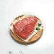 Raw Angus rump cap steak on butcher paper with parsley on a round wooden board