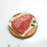 Raw Angus rump cap steak on parchment paper with parsley on a round wooden board