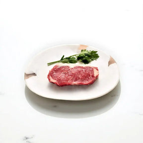 Raw Angus sirloin steak with herbs on a white ceramic plate, marble background