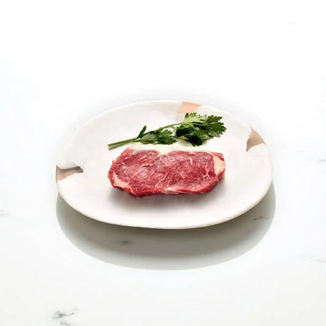 Raw Angus sirloin steak with parsley on a white ceramic plate, gourmet beef cut