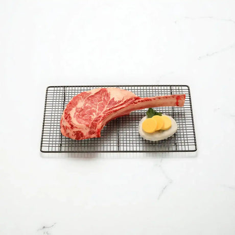 Premium Angus tomahawk steak by Peter Augustus Craft Butcher on wire rack with garnish