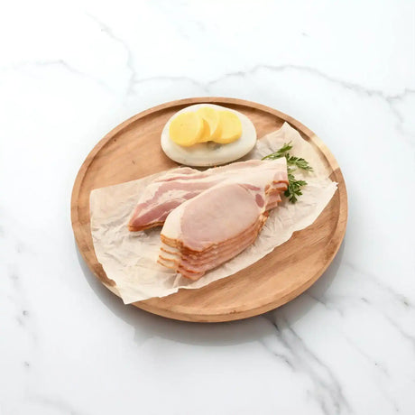 Sliced rindless bacon on parchment with garnish and butter on a wooden serving board