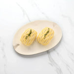 Two uncooked Peter Augustus beef Wellingtons with lattice pastry and herbs on a plate