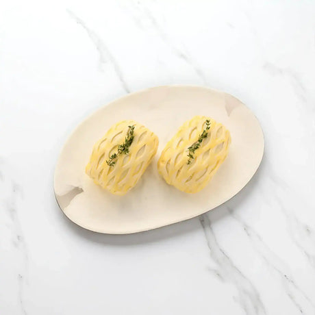 Two uncooked beef Wellingtons with lattice pastry and herbs on a plate, marble background