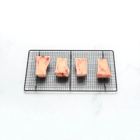 Four raw beef marrow bones on a black wire rack, isolated on a white background.