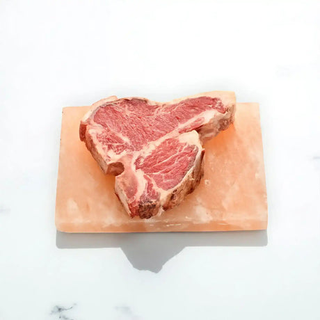 Dry aged Angus T-bone steak on a salt block, marbled beef on white background