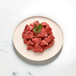Grass-fed diced beef pieces on a plate, garnished with parsley from Peter Augustus