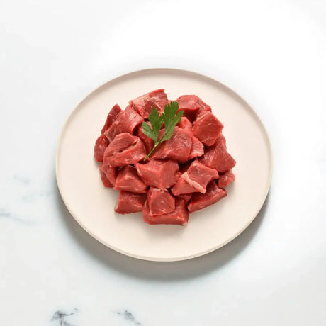 Fresh grass-fed diced beef pieces on a white plate, garnished with parsley