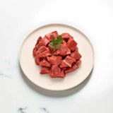Fresh grass-fed diced beef pieces on a white plate, garnished with a parsley leaf.