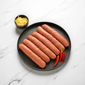 Six raw hot link sausages on a black plate with red chili peppers, shredded cheese on the side