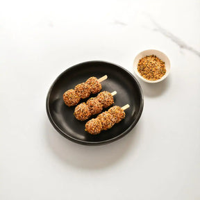 Seasoned lamb kofta skewers on black plate with spice mix in small bowl, white background