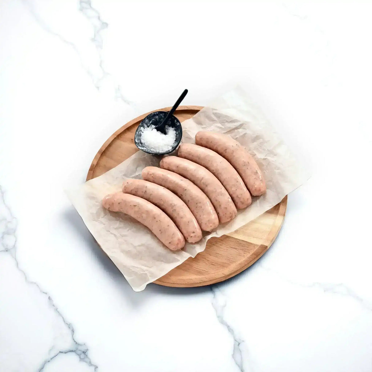 Raw pork truffle provolone sausages on parchment paper with salt bowl on wooden board