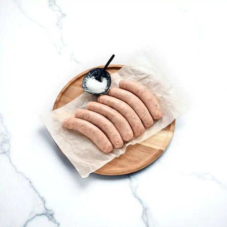 Raw pork sausages on parchment with sea salt on a round wooden board.