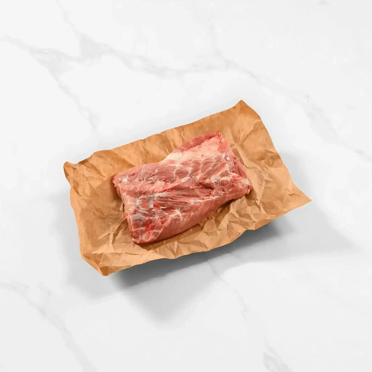 Raw pork collar butt steak on brown butcher paper, marble countertop background