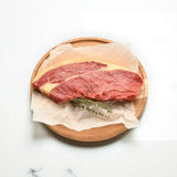 Raw rump steak on parchment paper with fresh herbs on a wooden board