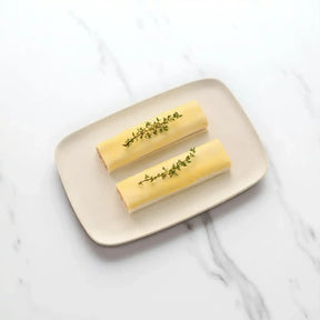 Two uncooked sausage rolls with pastry and fresh herbs on a beige plate, marble background