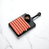 Thin BBQ beef sausages arranged on a black cutting board with a bowl of rock salt