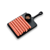 Black cutting board with hot dogs and a small bowl of spices