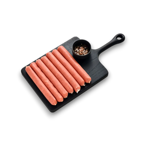 Black cutting board with hot dogs and a small bowl of spices