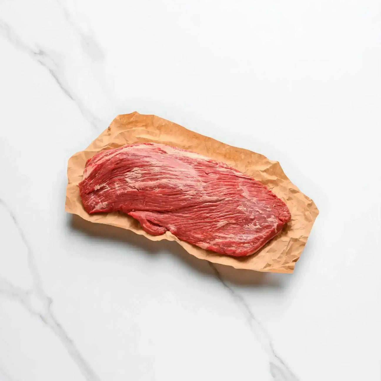 Raw Wagyu beef brisket on brown butcher paper, displayed on a white marble surface