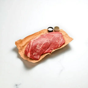 Raw Wagyu beef brisket on butcher paper with salt and pepper on a white background