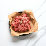 Fresh Wagyu diced beef cubes on brown paper in a bowl, garnished with rosemary