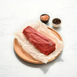Raw Wagyu eye fillet log on parchment paper with pink salt and peppercorns on a wooden plate