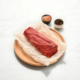 Raw Wagyu eye fillet log on parchment paper with pink salt and peppercorns on a wooden plate