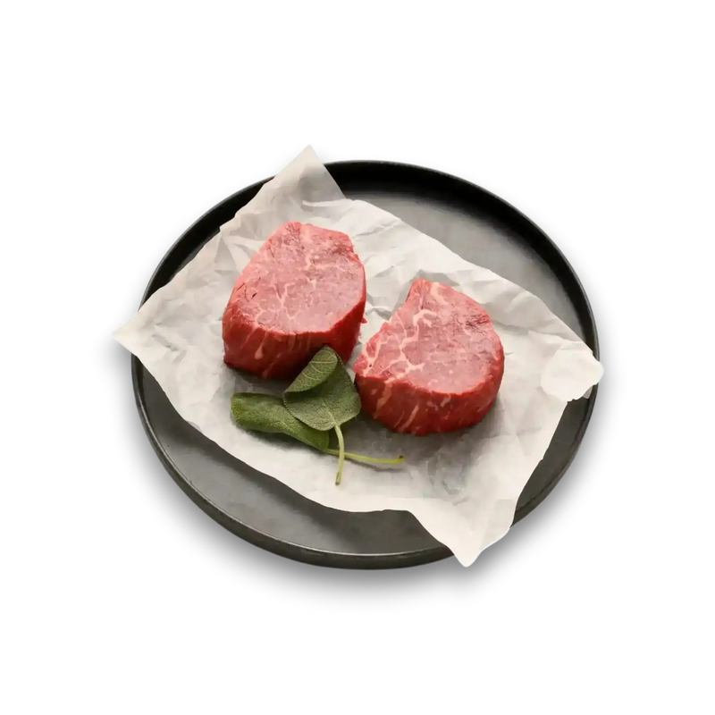 Two raw Wagyu beef fillets with marbling, served on parchment paper with fresh sage leaves on a black plate.