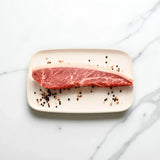 Raw Wagyu picanha steak with rich marbling on a ceramic plate with peppercorns