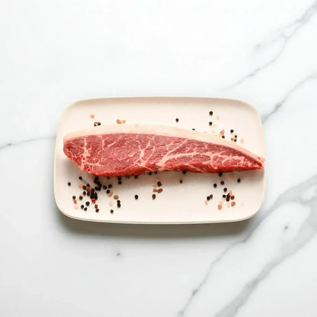 Raw Wagyu picanha steak with marbling on a plate, sprinkled with peppercorns and salt