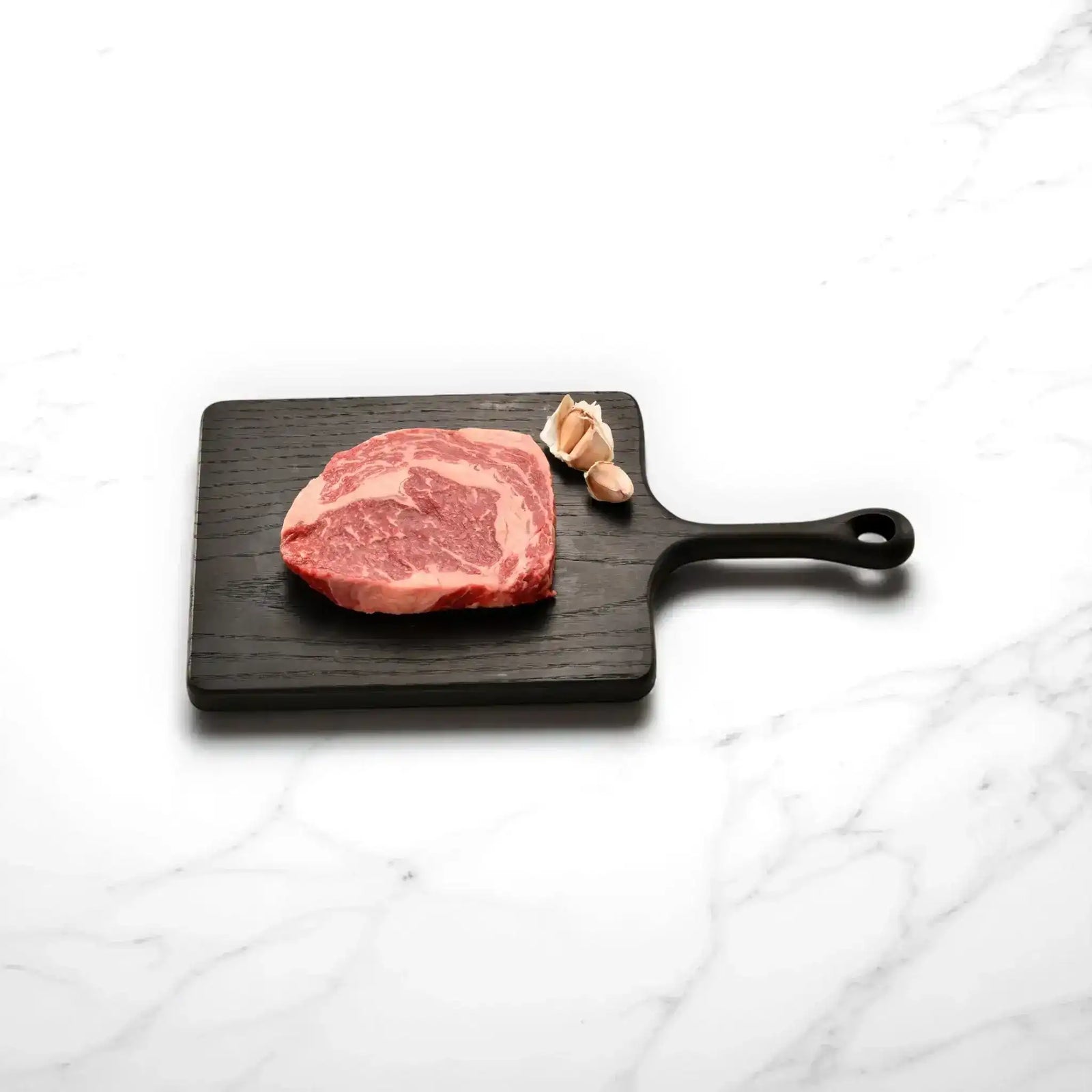 Marbled Wagyu rib fillet steak on wooden board with garlic, Peter Augustus premium Australian beef