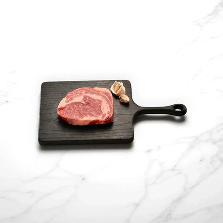 Raw Wagyu rib fillet steak with marbling on black board, garlic cloves, white marble background