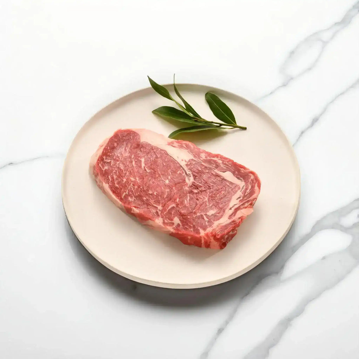 Raw Wagyu rib fillet steak with marbling on a plate, garnished with green leaves on marble