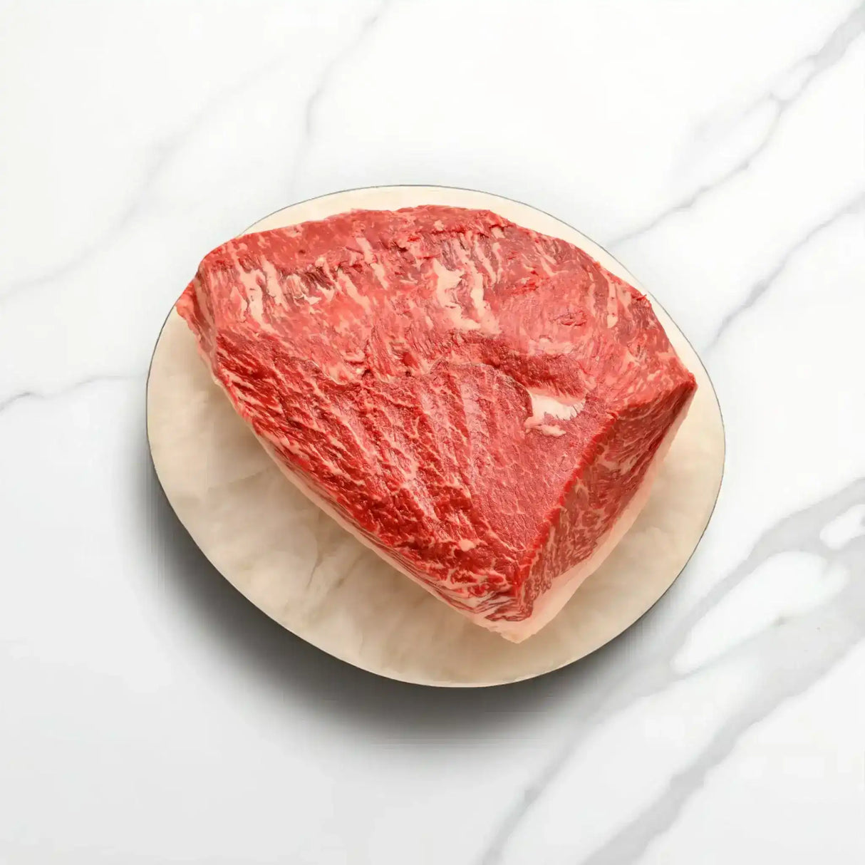 Raw Wagyu rump cap steak with marbling on a plate, isolated on a marble surface