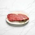 Raw Wagyu rump steak on a white plate with fresh herbs, marble background