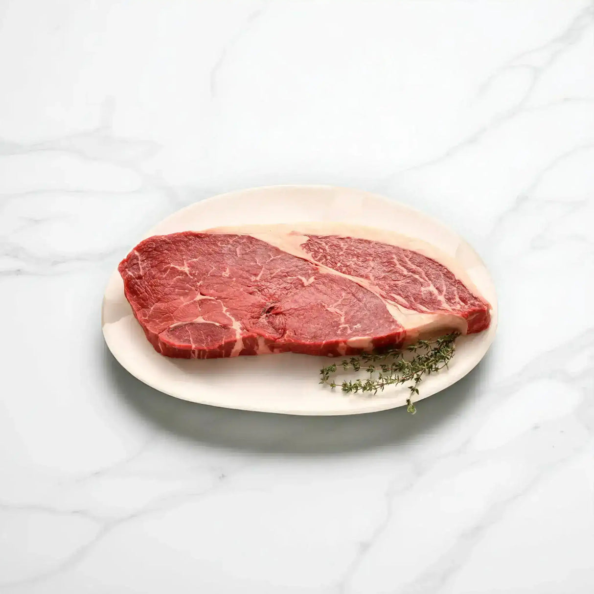 Raw Wagyu rump steak on a white plate with fresh herbs, marble background