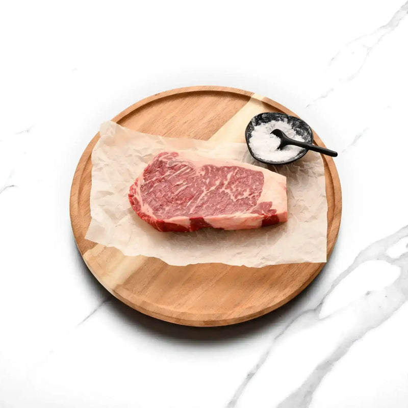 Marbled Wagyu sirloin steak on butcher paper with sea salt on a wooden board