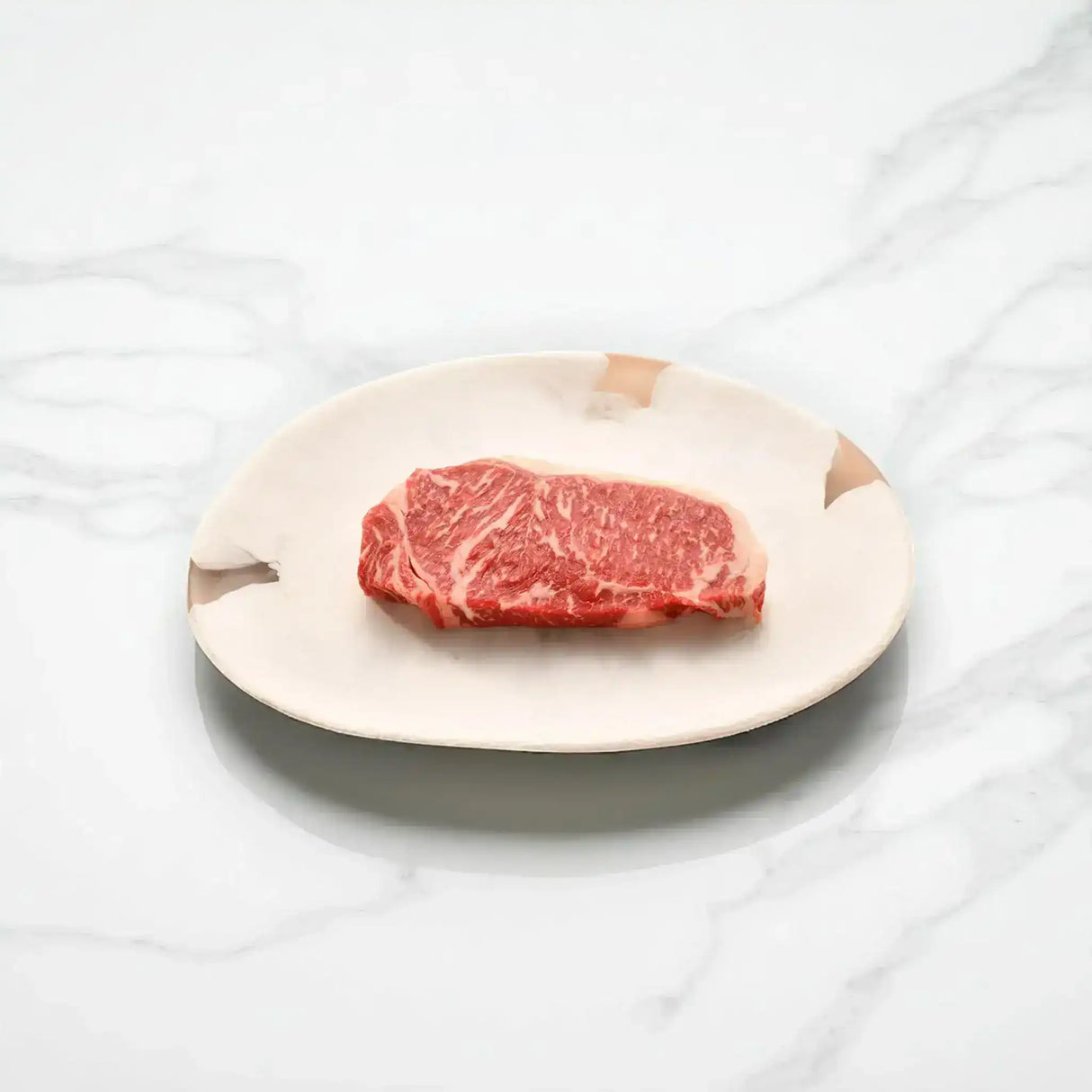 Raw Australian Wagyu sirloin steak with rich marbling on a ceramic plate, marble background