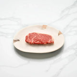 Raw Australian Wagyu sirloin steak with rich marbling on a ceramic plate, marble background