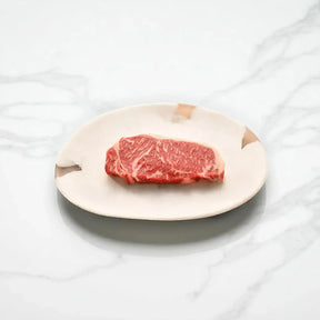 Raw Australian Wagyu sirloin steak with rich marbling on a ceramic plate, marble background