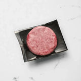 Vacuum-sealed raw beef burger patty on black tray, marble surface background
