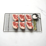Six fresh lamb loin chops on a wire rack with rosemary and a small bowl of sea salt
