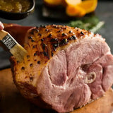Glazed and roasted Christmas ham with cloves being brushed with sauce on a wooden board