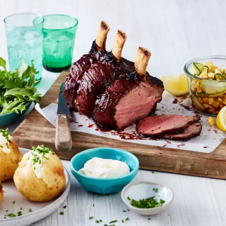 Succulent roast beef rib on a board, served with baked potatoes, salad, and corn relish.