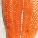 Fresh raw salmon fillet with vibrant orange color and visible marbling on white paper