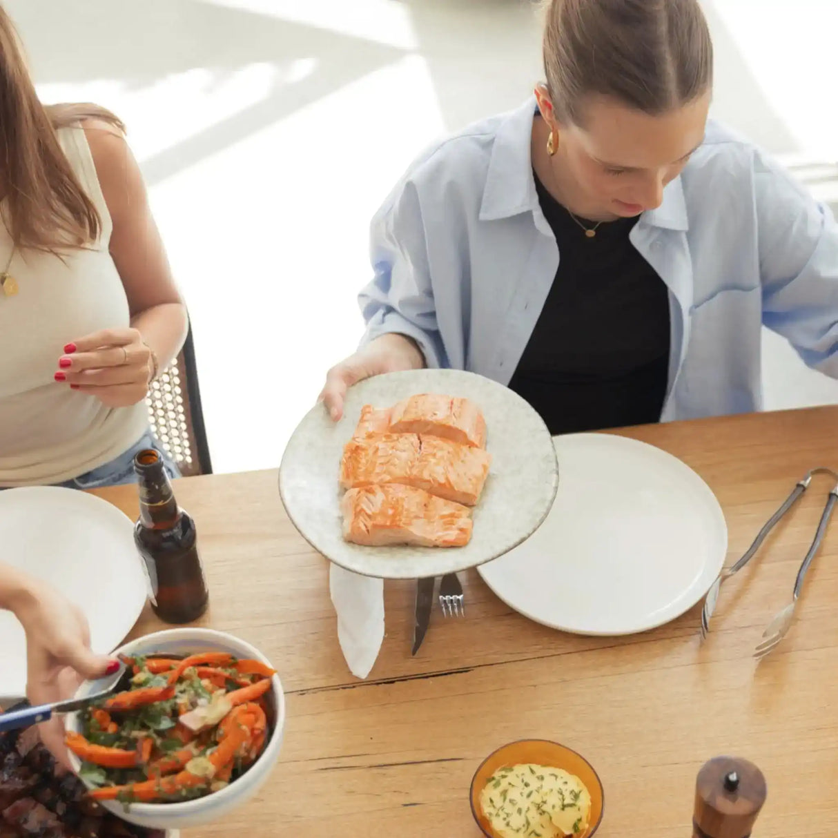 Woman serving grilled salmon fillets at a dinner table with salad and sauce