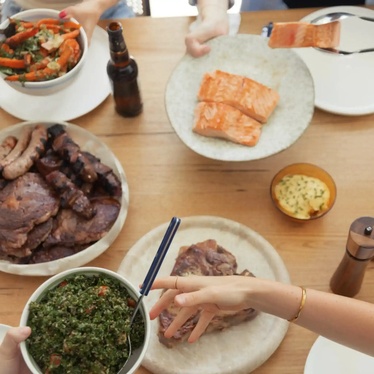 Table with grilled beef, sausages, salmon fillets, salad, and herb butter