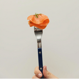 Hand holding fork with sliced smoked salmon garnished with dill against white background