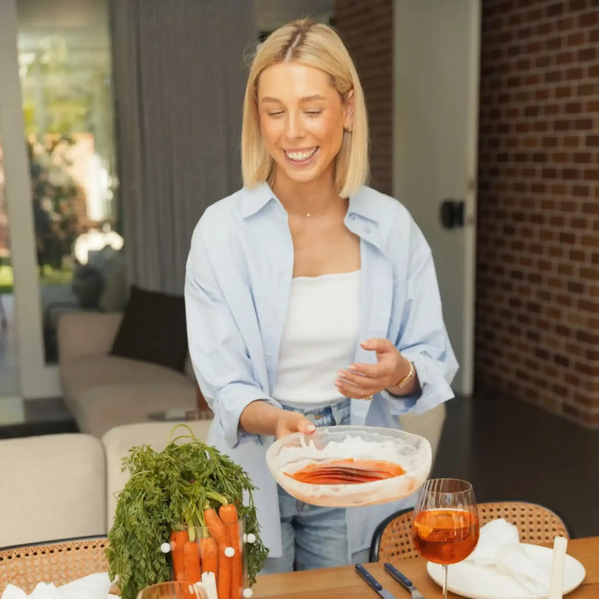 Smiling woman holding marinated salmon in a modern kitchen with fresh carrots on table